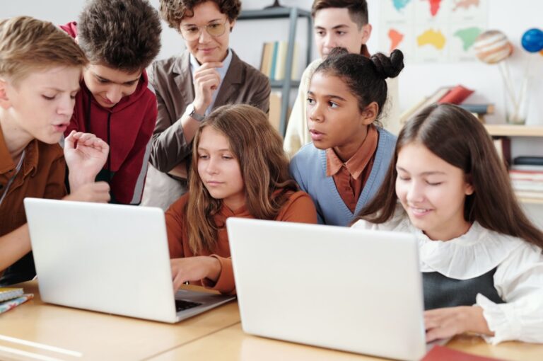 Young students in a classroom gathered around laptops