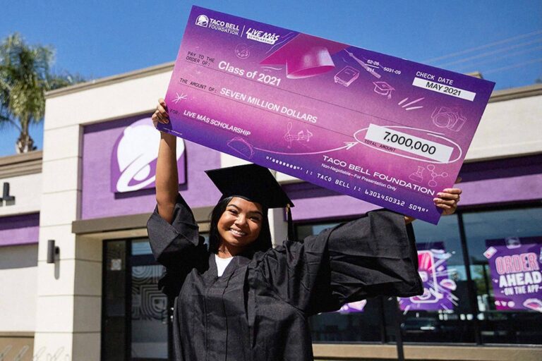 Woman in graduation robes with Taco Bell Foundation check