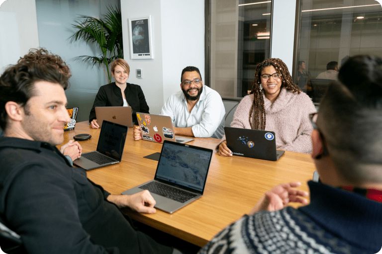 Smiling coworkers sitting around a table with laptops